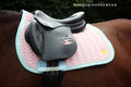 SAMPLE Saddle pad in light pink with light blue and minty details, golden logo, under black jumping saddle on horse