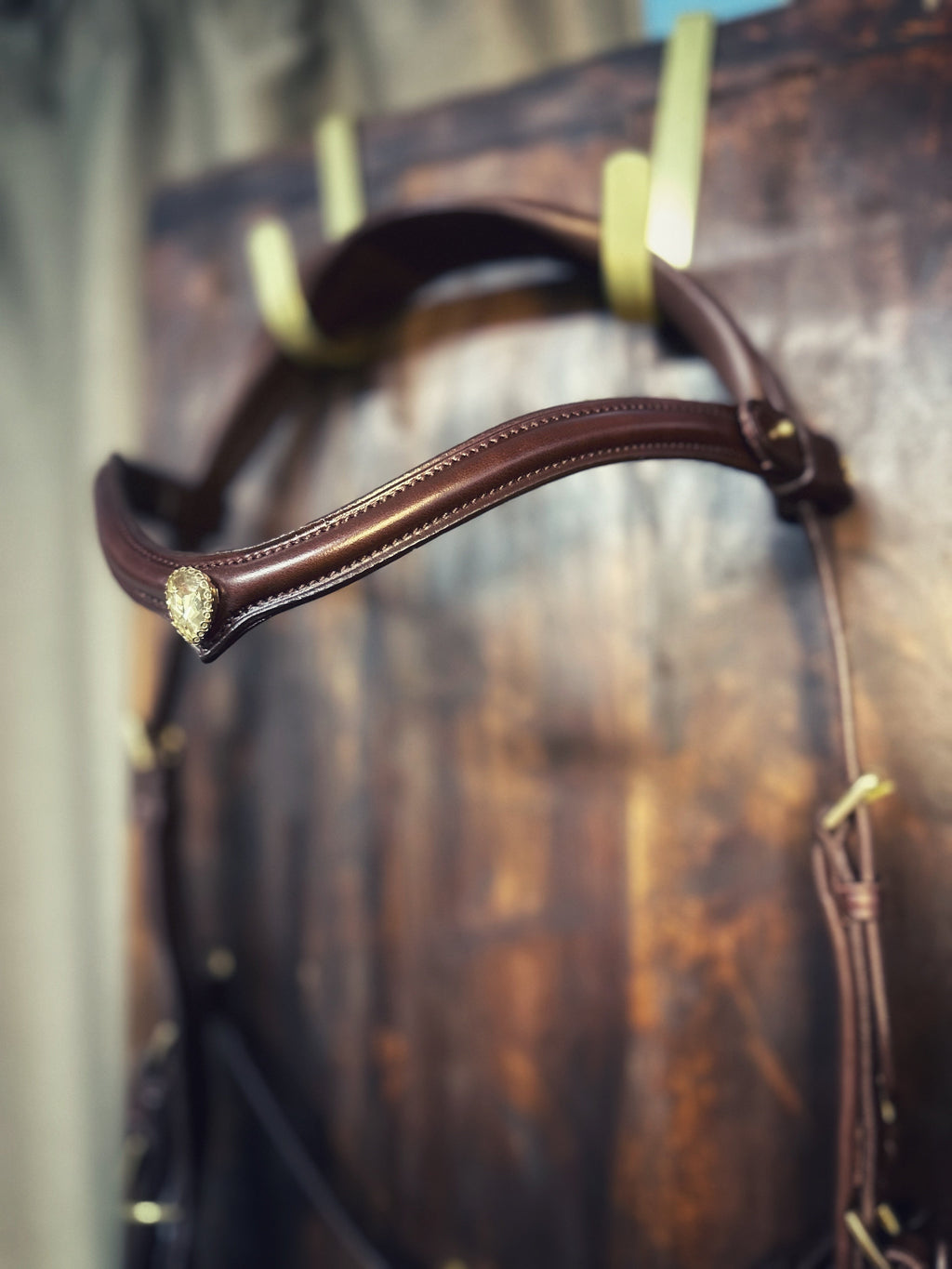 Brown Stella browband made of Italian leather with golden crystal and brass details hanging on wooden wall